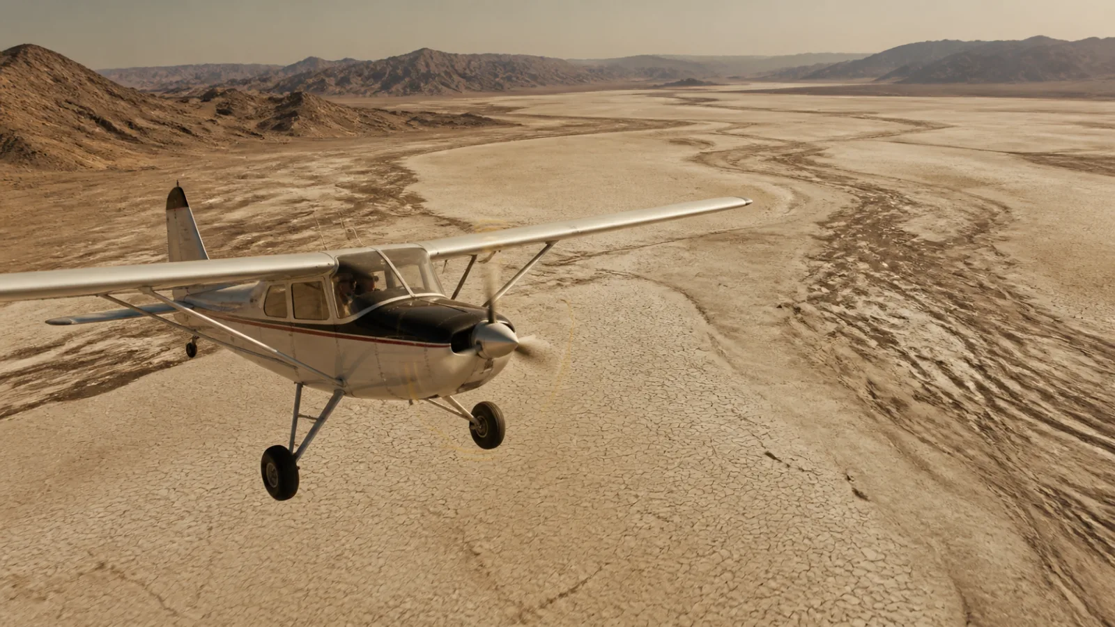 Small propeller survey aircraft flying low over a dry cracked lakebed while scouting the terrain below