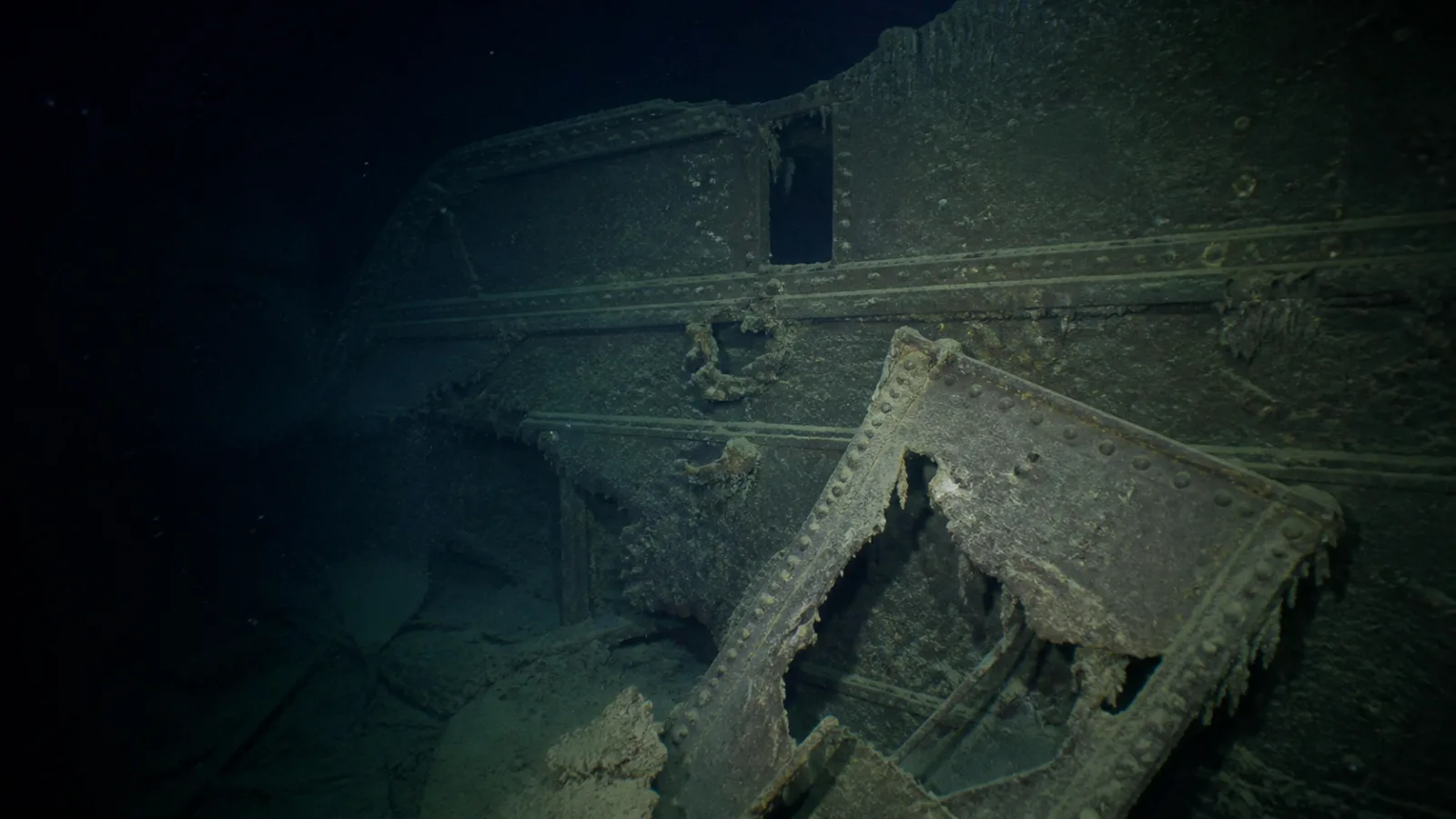 Submersible lights illuminate rusted shipwreck debris on the dark ocean floor
