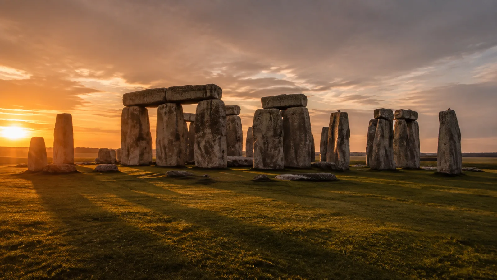 Stonehenge at golden dusk with long shadows stretching across the grass