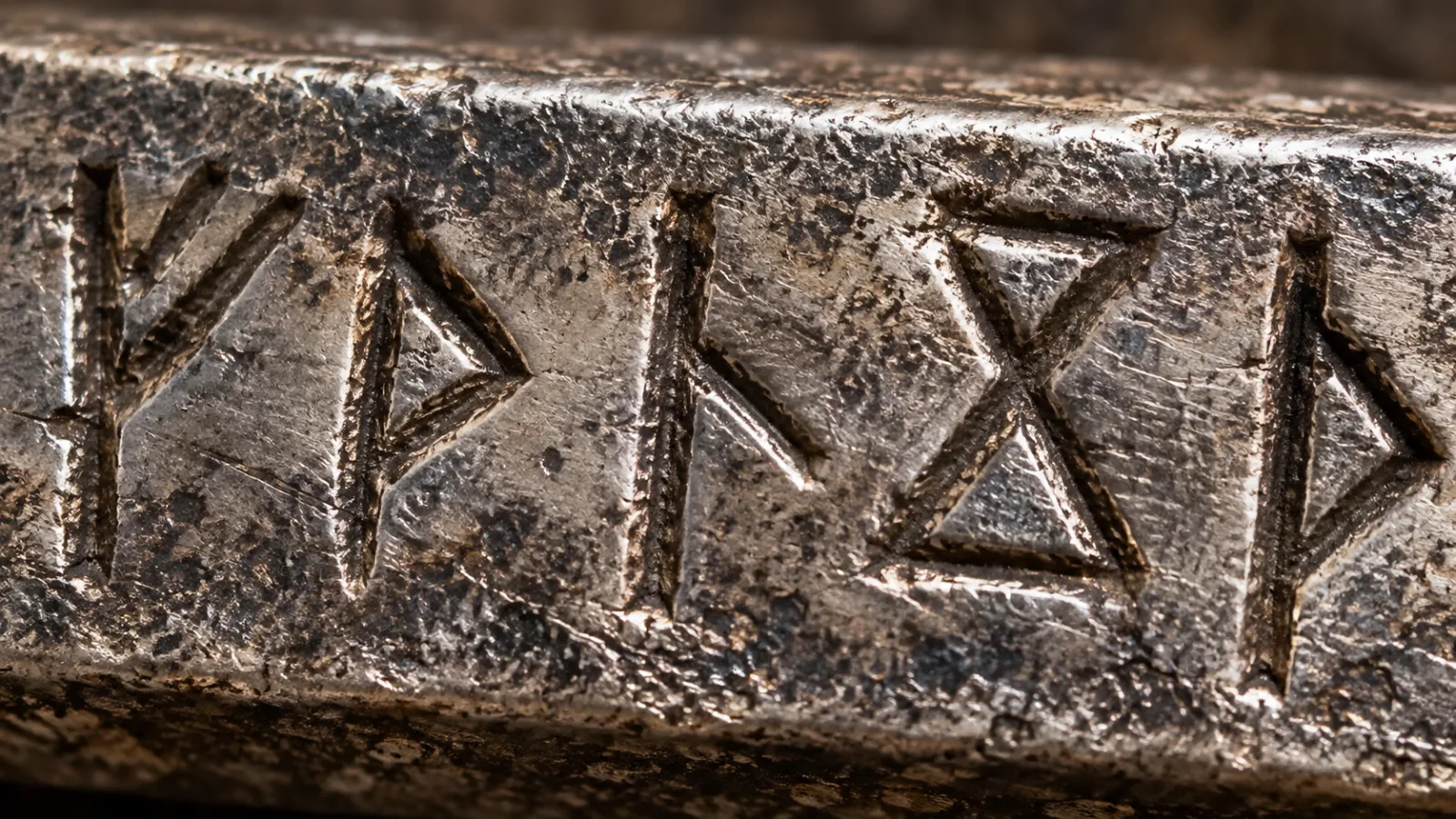 Macro photograph of runic symbols carved into a tarnished silver bar