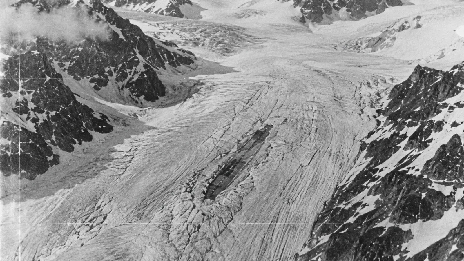 Grainy black-and-white style recreation of an aerial reconnaissance photo showing a linear shape in mountain ice