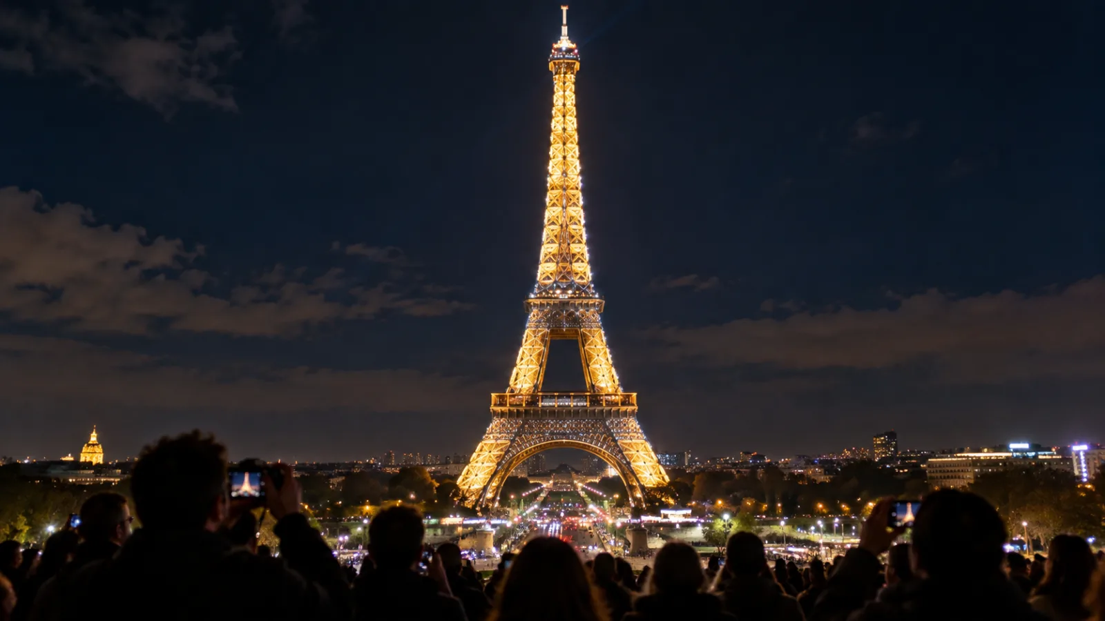 Nighttime view of the illuminated Eiffel Tower sparkling against a dark sky with tourists below